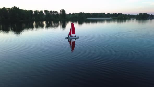 Flying Around a Catamaran Floating on the River with Scarlet Sails at Sunset