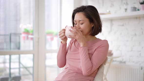 Asian mix race woman enjoying cup of coffee or tea drinking warm beverage at home