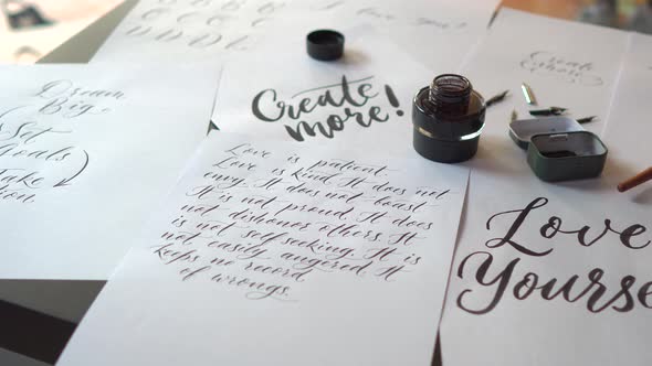 Closeup Shot of a Calligraphy Tools and a Bottle of Ink and Sheets of Paper with Different Writings alt