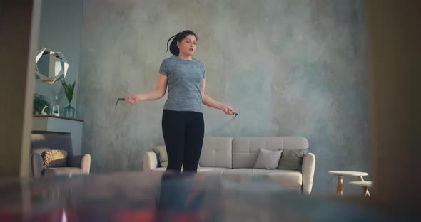Stylish Lady Jumps Rope Training Near Sofa in Living Room alt