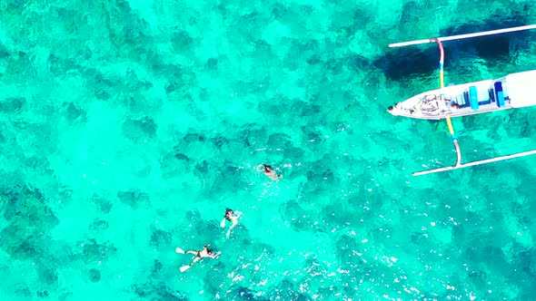 Group of people snorkeling in the aquamarine sea water near the fishing boat. alt