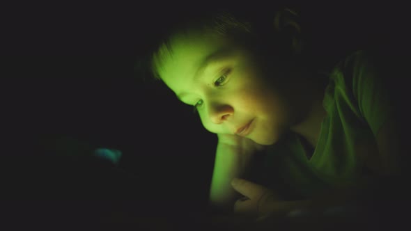 Little Boy Watches Cartoons in the Tablet Late in the Evening Closeup Face alt