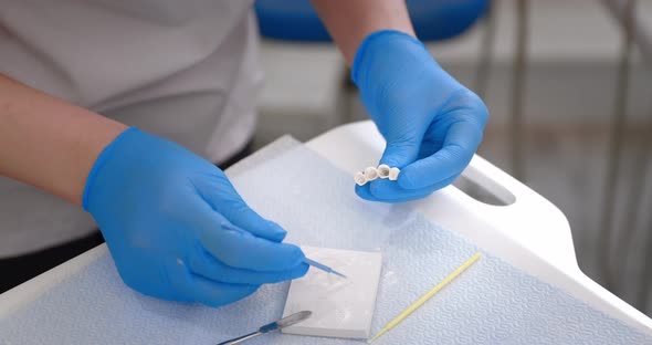 Hands of a Dentist in Medical Gloves Work with Dental Implants and Crowns in a Medical Office alt