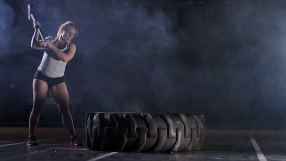 Strong Confident Fitness Woman Hitting Large Tractor Tire with Sledgehammer