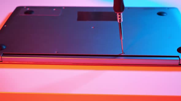 Unrecognizable Master Screwing Bolts Into Laptop Lid in Muted Red and Blue Light alt