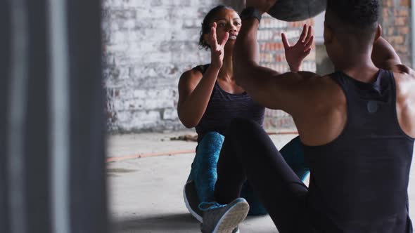 African american man and woman exercising with medicine ball in an empty urban building alt
