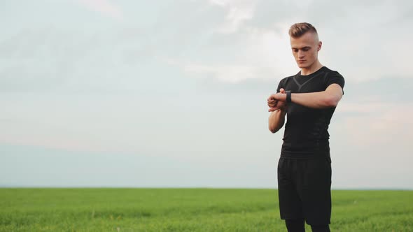 The Athlete is Standing on the Field and Choosing the Type of Training on His Watch alt