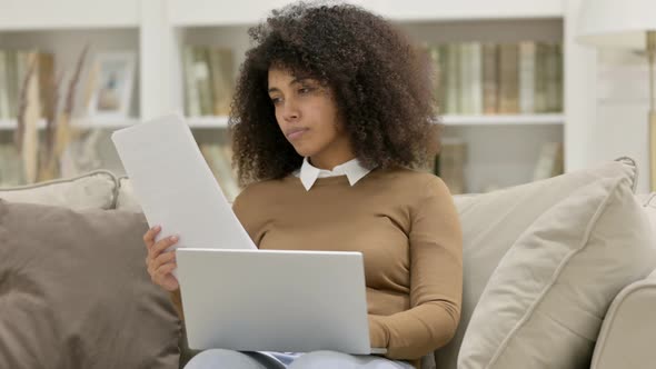 Young African Woman with Documents Working on Laptop on Sofa alt