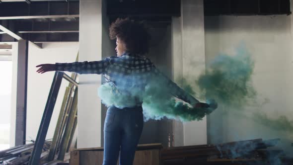 Mixed race woman holding green flare dancing in an empty building alt