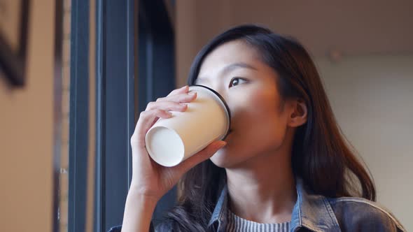 Businesswoman drinking coffee looking outside the window at the office.