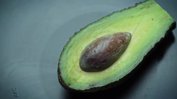 Half of an Avocado with a Stone Rotates in a Circle on a Black Background alt