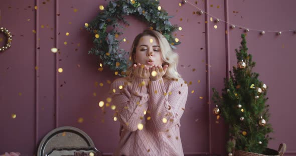 Beautiful Woman in Sweater Blows Shiny Confetti From Her Hands To the Camera in Slow Motion alt