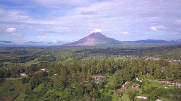 Reverse drone shot of Mount Sinabung volcano and the surrounding beautiful green village in Berastag alt