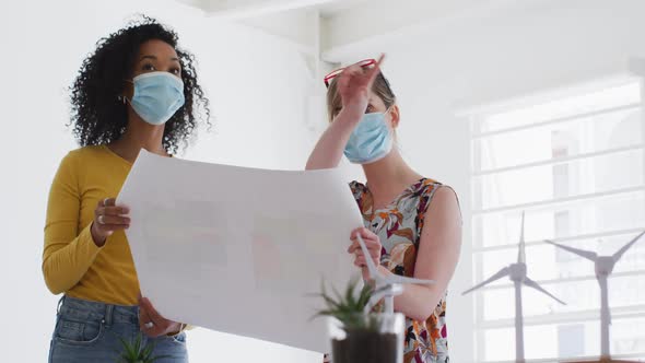 Two woman wearing face mask discussing over document at office alt