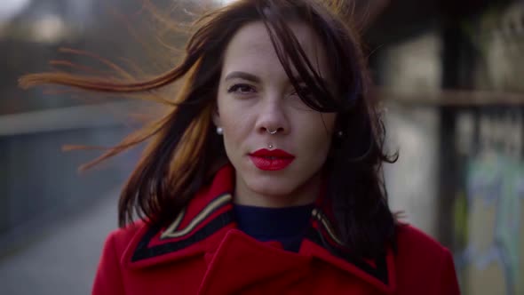 Portrait of a Brunette with a Bright Make-up and Piercing on Her Face. She Is Dressed in a Red alt