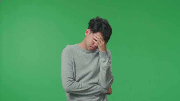 Asian Man Having Headache While Standing In Front Of Green Screen Background alt