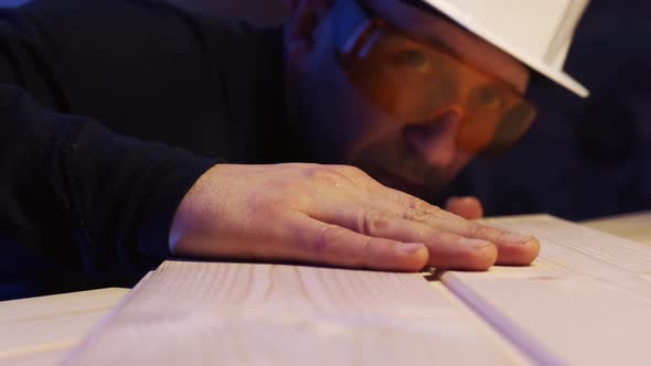 A Male Construction Worker in a Protective Helmet Runs His Hand Over the Board