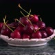 Fresh red sweet cherries in bowl. Ripe wet cherry berries rotate on black.