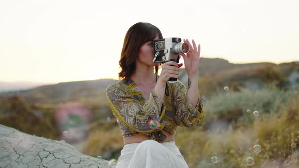 Young Girl Shoots with the 8Mm Vintage Camera in the Nature Among the Bubbles alt