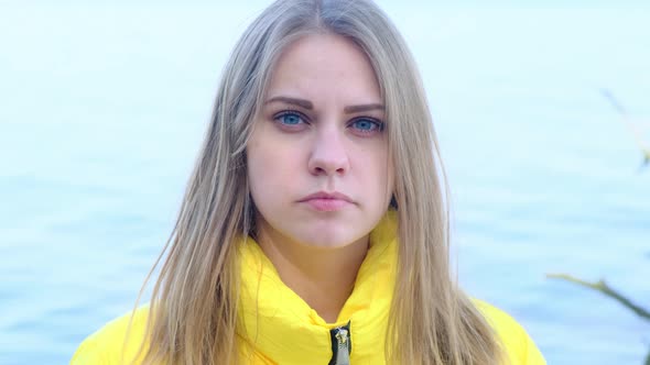 Portrait of a Sad Serious Young Woman Looking Into the Camera Against the Background of the River in