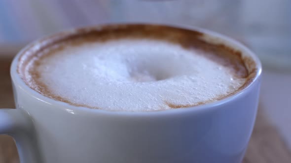 Woman stirs with a spoon the thick foam of hot cappuccino coffee in a glass cup. alt