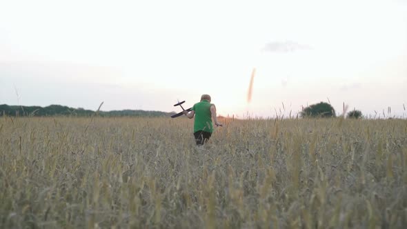 A Boy with an Airplane in His Hands Is Running in the Field
