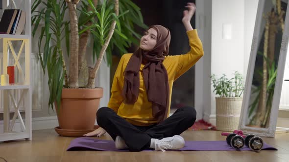 Wide Shot Front View of Fit Woman in Hijab Warming Up Muscles Sitting on Exercise Mat Training at alt