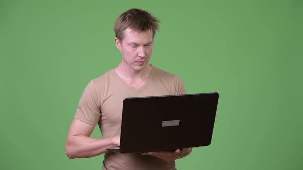 Young Happy Scandinavian Man Thinking While Using Laptop alt