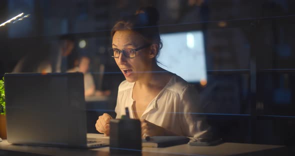 Happy Businesswoman Celebrating Success and Working on Computer at Night in Office alt