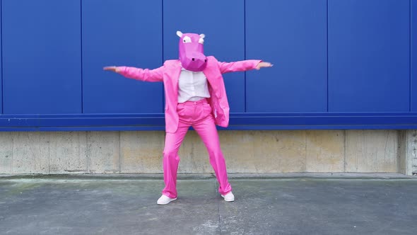 Businesswoman wearing hippo mask dancing in front of blue wall alt
