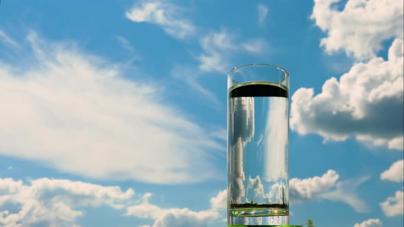 Pour Water Into A Transparent Glass With Time Lapse On The Background Of The Sky