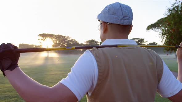 Golfer carrying golf club over shoulder while standing on the golf course alt