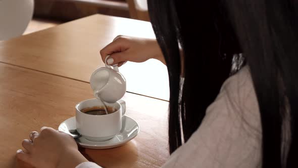 Girl Adds Cream Into Her Coffee at the Cafe