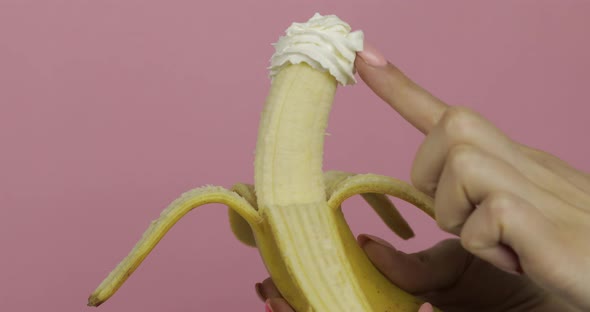 Woman Hand Holds Banana with Whipped Cream on Fruit. Finger Touches the Cream alt