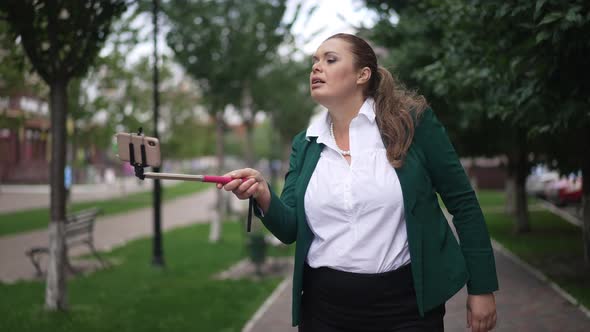 Positive Overweight Female Business Blogger Standing in City Talking Smiling Waving Greeting alt