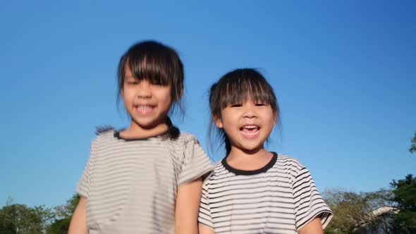 Happy Asian siblings girls hugging each other in the summer garden on a bright sky background. alt