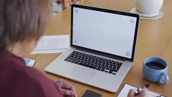 African american senior woman at dining table, using laptop with copy space on screen and writing alt