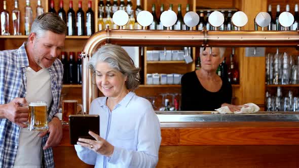 Friends using digital tablet while having beer at counter 4k alt