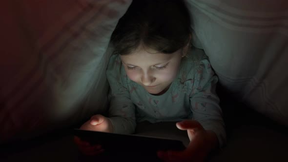 little girl using a cell phone at night. hiding under a blanket