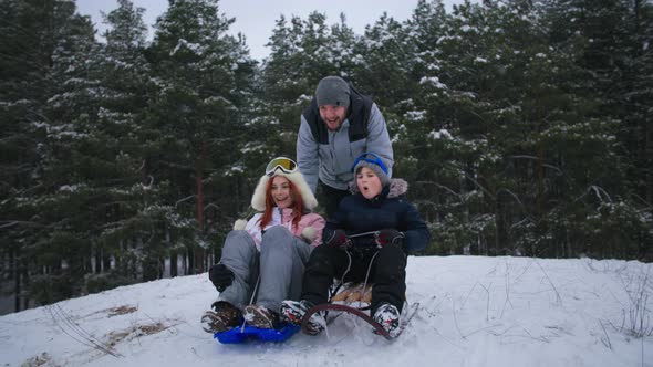 Active Weekend Happy Father Sledding His Son and Woman Down a Snowy Hill in Winter Forest