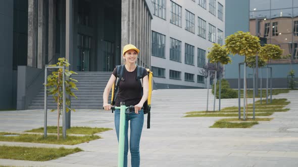 Portrait Lady Delivery Worker with Backpack and Yellow Cap Rides Electric alt