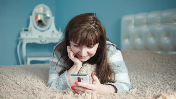 Brunette Woman Lies on the Bed and Uses the Phone Chat with Friends in Love Received a Message From alt