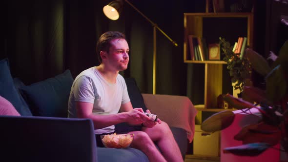 Young Man Gamer Playing Video Game on Tvand Eating Snack Chips in Evening alt