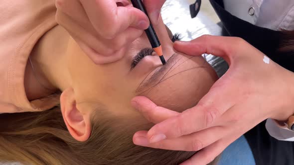 Cosmetologist Draws a Contour of Eyebrows on a Young Girl