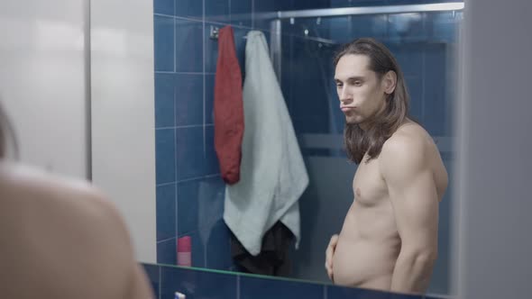 Young Naked Man Sucking in His Belly Whishing to Be Fitter  Middle Shot alt