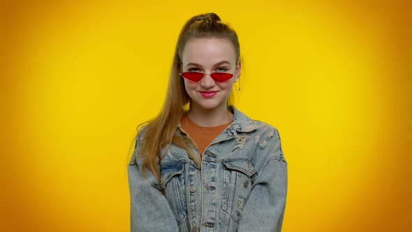 Sincere Cool Cheerful Stylish Girl in Denim Jacket Wearing Sunglasses Charming Smile on Yellow Wall alt