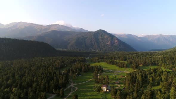 Aerial View a Farm in a Clearing in the Forest Against the Backdrop of Mountains alt