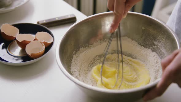 Person Preparing Homemade Omelette Mixing Eggs with Hand Corolla. alt
