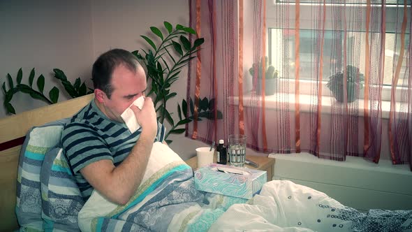 Ill Man Blowing Nose with Wipe Lying in Bed at Home