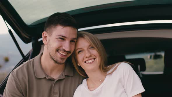 Young Traveler Couple on Road Trip in Mountains Sitting in a Trunk of a Car